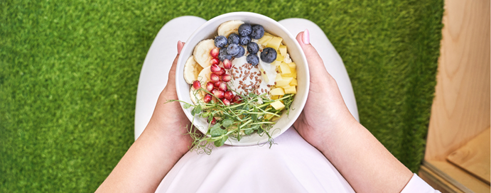 Raskaana oleva nainen pitelee jogurttikulhoa sylissään