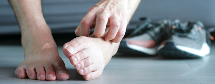 Paljain jaloin oleva henkilö tutkii jalkojaan harmaalla lattialla, lenkkarit taustalla.