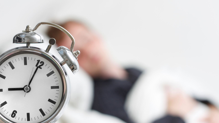 Herätyskello sängyn vierellä. Kuvituskuva