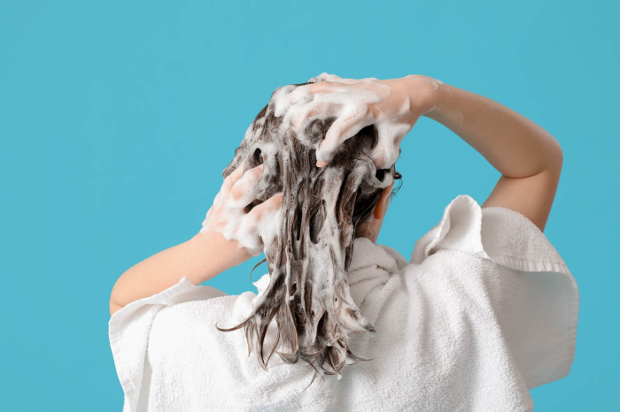 Nainen pesemässä hiuksiaan shampoolla. Sininen tausta.