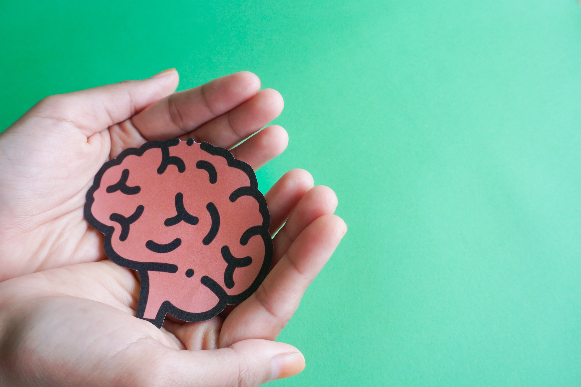 Dementia ja alzheimerin tauti - naisen kädet pitämässä paperisia aivoja vihreällä taustalla