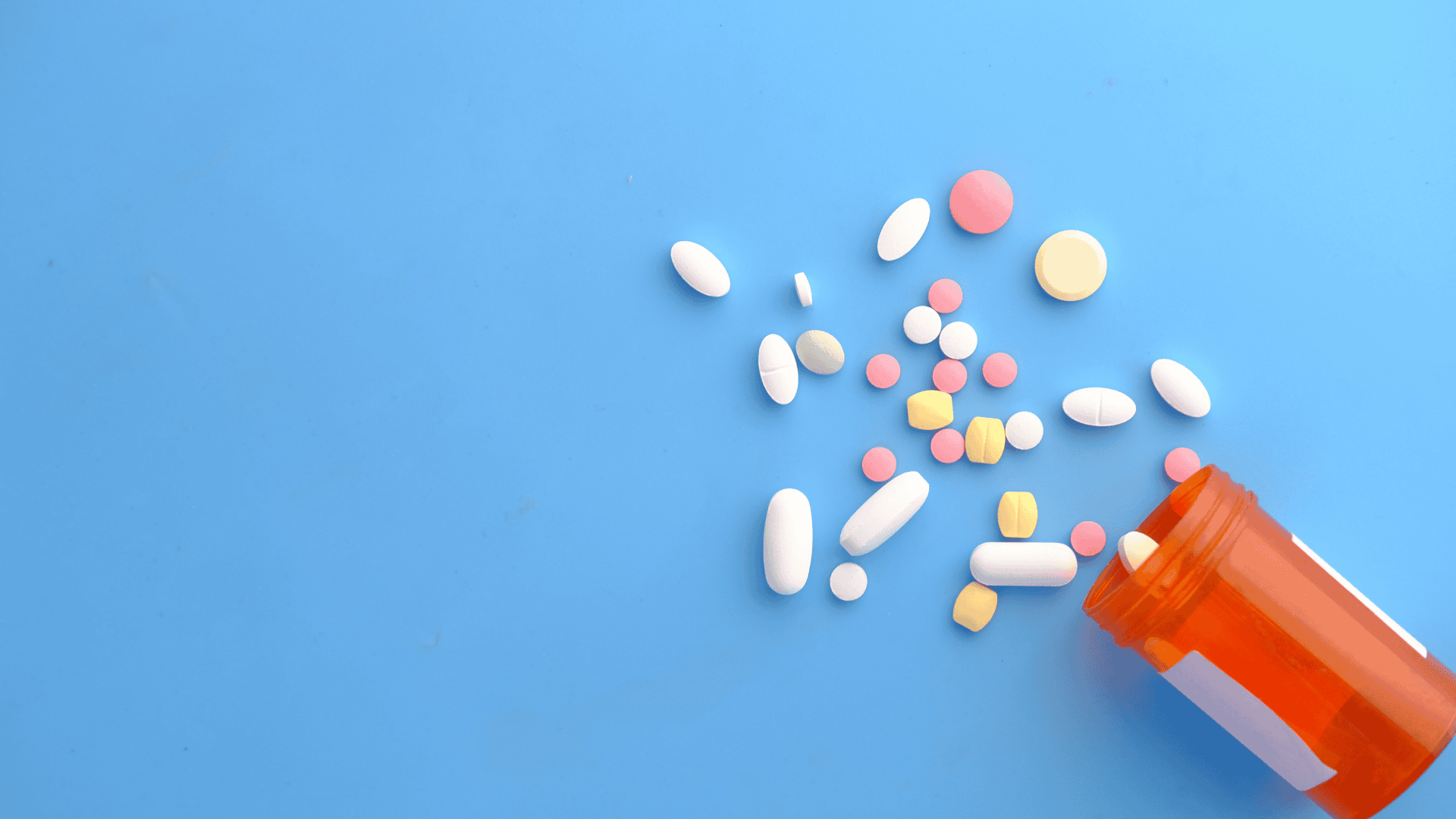 Kuvituskuva; siniselle taustalle levinnyt geneerinen lääkepurkki ja erivärisiä pillereitä.