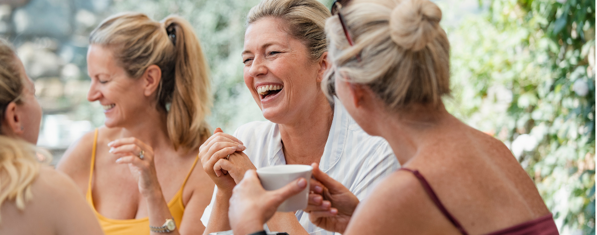 nauravia naisia istumassa pöydän ääressä, kahvikuppi kädessä